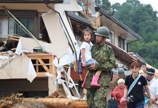 倒壊した家屋を背に、自衛隊員に抱きかかえられながら避難する女児＝６日午後０時４５分、福岡県朝倉市（恵守乾撮影）